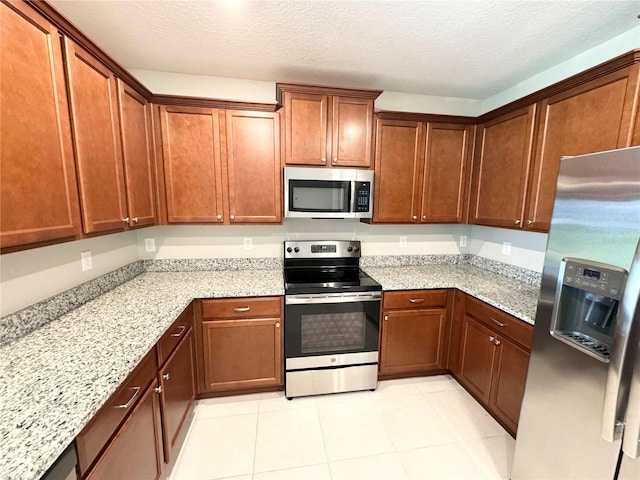 kitchen with light stone counters, a textured ceiling, stainless steel appliances, and light tile patterned floors