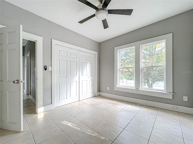 unfurnished bedroom featuring a closet, ceiling fan, a textured ceiling, and light tile patterned floors