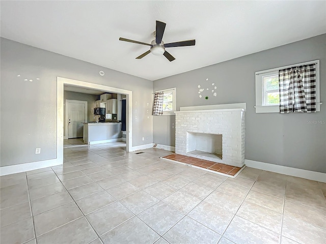 unfurnished living room with a brick fireplace, light tile patterned floors, and plenty of natural light