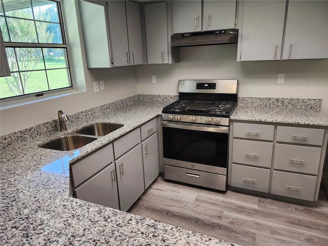 kitchen featuring gray cabinetry, light stone countertops, light wood-type flooring, gas stove, and sink