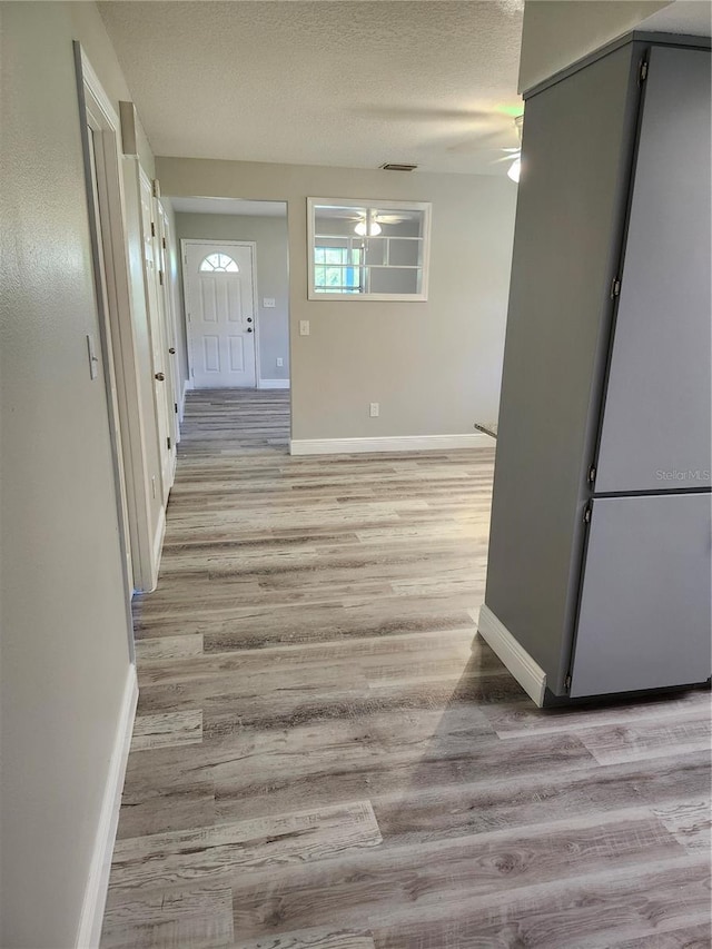 hall with a textured ceiling and light hardwood / wood-style flooring