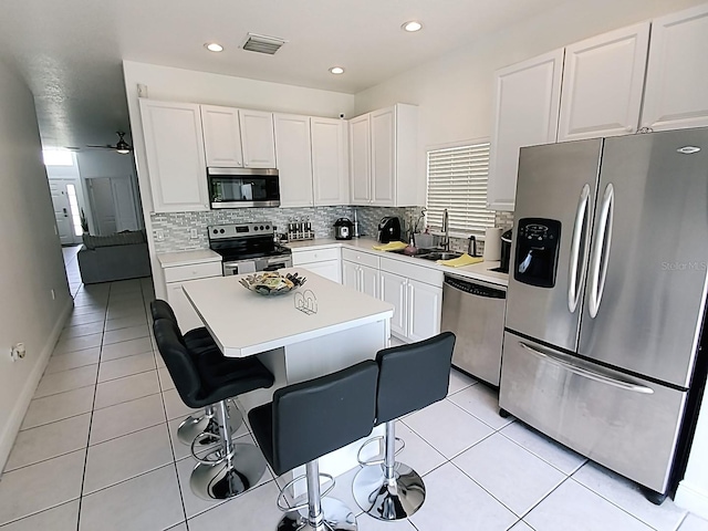 kitchen with appliances with stainless steel finishes, white cabinetry, a breakfast bar, a kitchen island, and sink