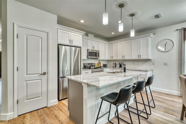 kitchen with light hardwood / wood-style floors, white cabinets, pendant lighting, stainless steel appliances, and sink