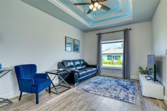 living room with wood-type flooring, a tray ceiling, ornamental molding, and ceiling fan