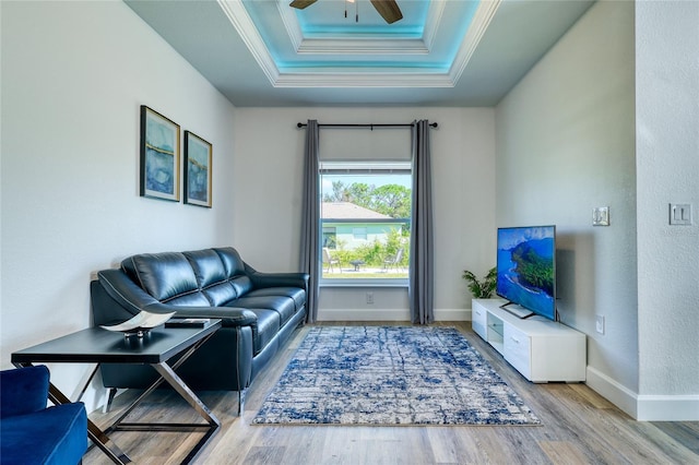 living room with light wood-type flooring, ceiling fan, a raised ceiling, and crown molding