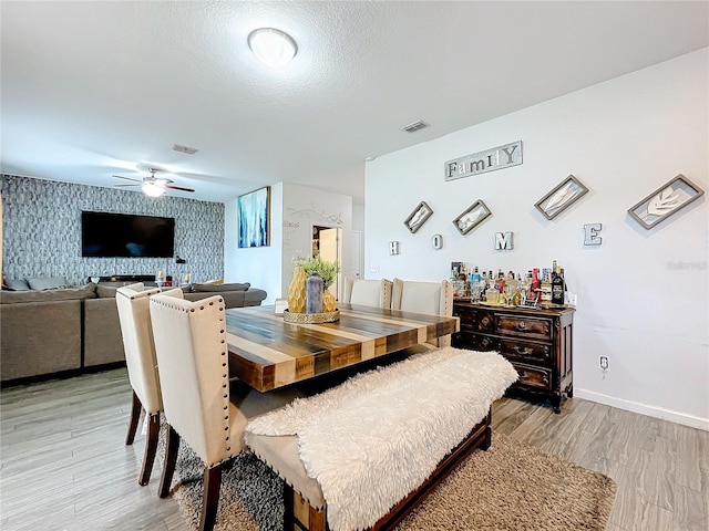 dining area featuring light wood-type flooring, a textured ceiling, and ceiling fan