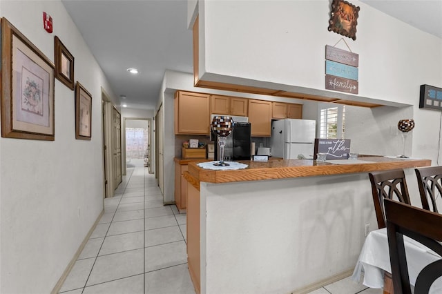 kitchen with black fridge, light tile patterned flooring, kitchen peninsula, white fridge, and a kitchen breakfast bar