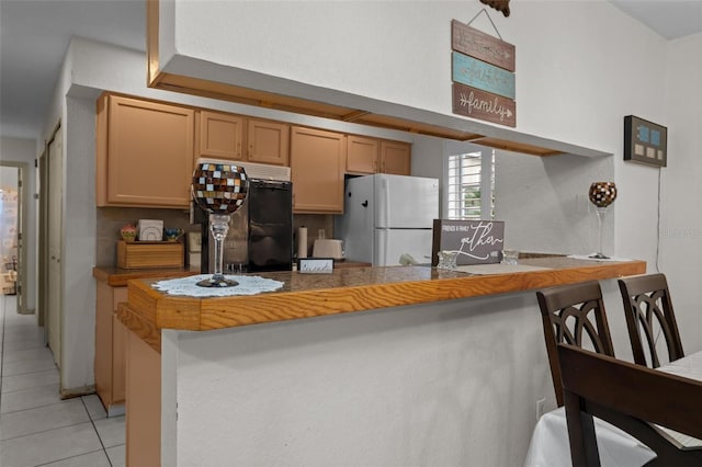 kitchen with black fridge, light tile patterned floors, kitchen peninsula, a kitchen breakfast bar, and white fridge