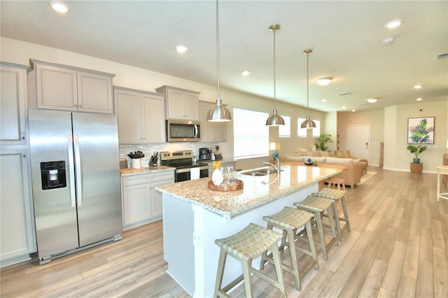 kitchen with appliances with stainless steel finishes, a center island with sink, a breakfast bar area, and light stone counters