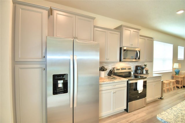 kitchen featuring light wood-type flooring, light stone countertops, stainless steel appliances, and tasteful backsplash