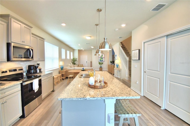 kitchen with light hardwood / wood-style floors, a kitchen island with sink, stainless steel appliances, and decorative light fixtures