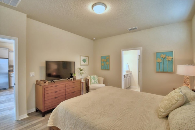 bedroom featuring light wood-type flooring, stainless steel fridge, a textured ceiling, and ensuite bath