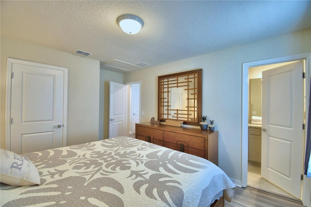 bedroom featuring a textured ceiling, ensuite bath, and light hardwood / wood-style flooring