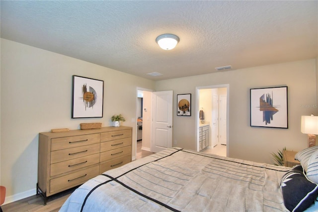 bedroom with a textured ceiling, light hardwood / wood-style floors, and ensuite bathroom