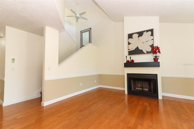 unfurnished living room with a tile fireplace, ceiling fan, hardwood / wood-style floors, and a textured ceiling