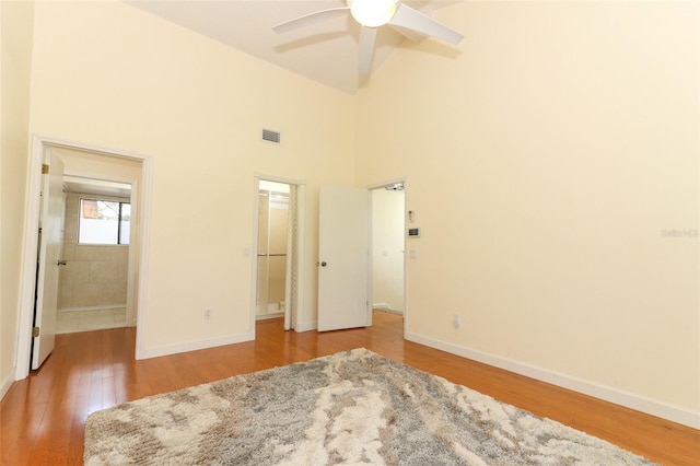 unfurnished bedroom featuring connected bathroom, ceiling fan, a high ceiling, light hardwood / wood-style floors, and a walk in closet