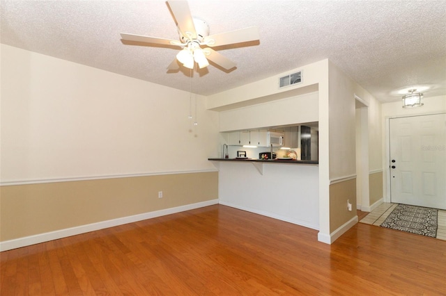 unfurnished living room featuring ceiling fan, wood-type flooring, and a textured ceiling