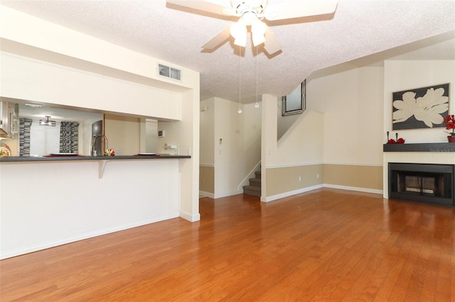 unfurnished living room with a textured ceiling, hardwood / wood-style flooring, ceiling fan, and sink