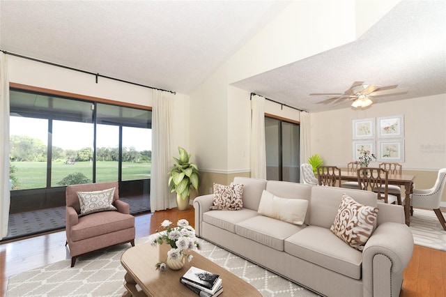 living room featuring ceiling fan, light wood-type flooring, a textured ceiling, and vaulted ceiling