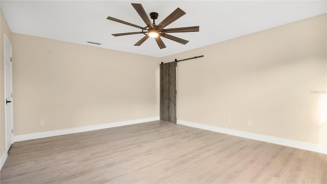 empty room with light wood-type flooring, ceiling fan, and a barn door