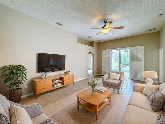 living room with ceiling fan, a textured ceiling, and light wood-type flooring