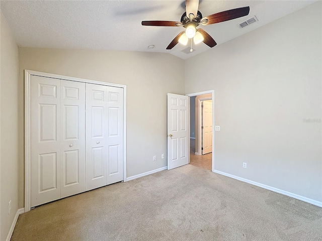 unfurnished bedroom with a textured ceiling, light colored carpet, vaulted ceiling, ceiling fan, and a closet