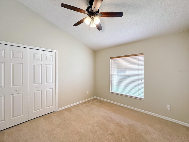 unfurnished bedroom featuring a textured ceiling, light colored carpet, vaulted ceiling, ceiling fan, and a closet