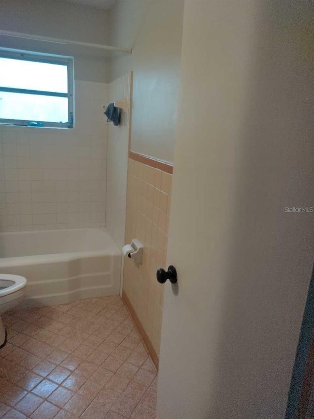 bathroom with tile patterned flooring, tiled shower / bath combo, and toilet