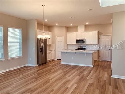 kitchen featuring appliances with stainless steel finishes, hanging light fixtures, white cabinetry, light hardwood / wood-style flooring, and a kitchen island with sink