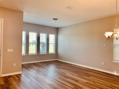 unfurnished room featuring a notable chandelier and dark hardwood / wood-style floors