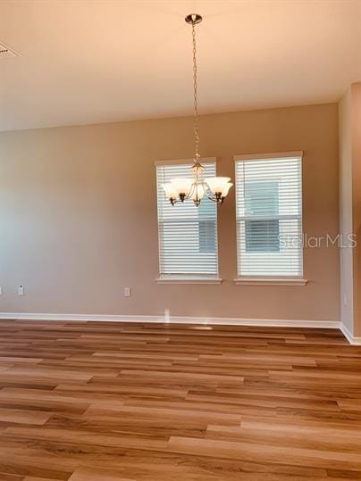 spare room featuring wood-type flooring and an inviting chandelier