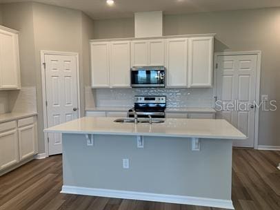 kitchen featuring appliances with stainless steel finishes, white cabinetry, dark hardwood / wood-style flooring, and an island with sink