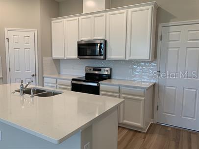 kitchen with appliances with stainless steel finishes, decorative backsplash, white cabinetry, an island with sink, and sink