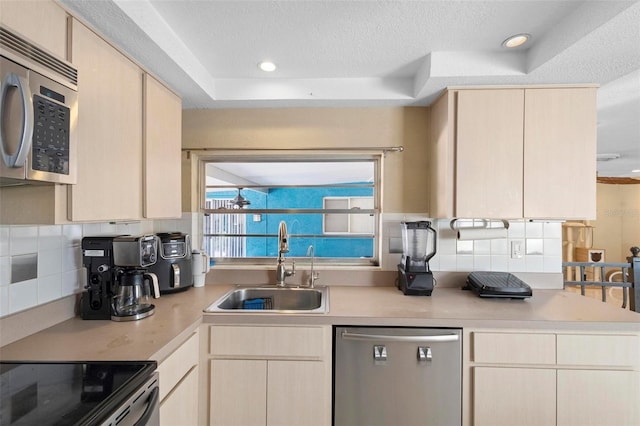 kitchen with a tray ceiling, a textured ceiling, sink, appliances with stainless steel finishes, and light brown cabinetry