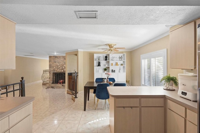 kitchen featuring light tile patterned flooring, kitchen peninsula, a fireplace, crown molding, and light brown cabinetry