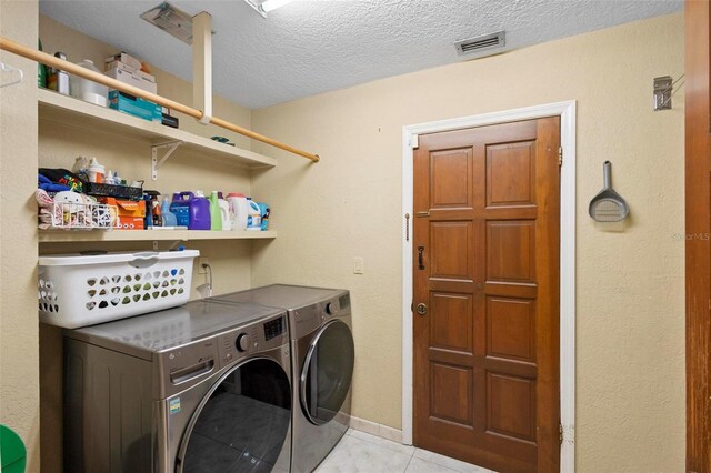 laundry room featuring light tile patterned floors, washer and clothes dryer, and a textured ceiling