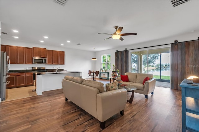 living room featuring sink, dark wood-type flooring, a barn door, and ceiling fan