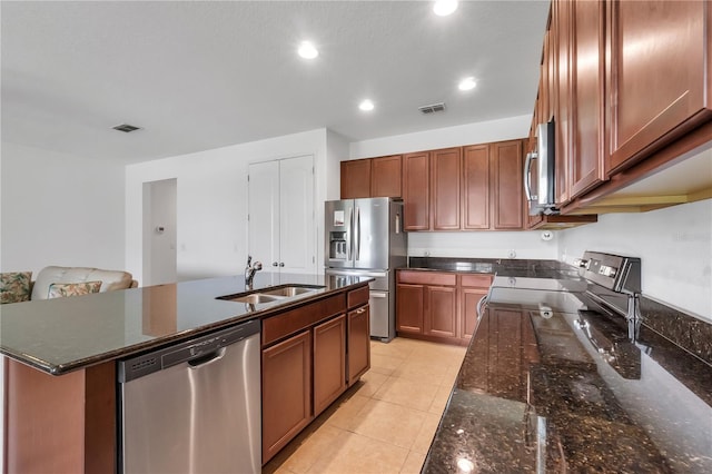 kitchen featuring sink, appliances with stainless steel finishes, a kitchen island with sink, and dark stone counters