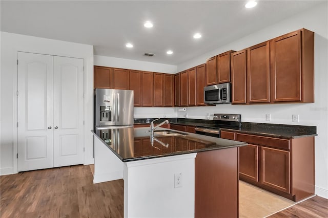 kitchen with appliances with stainless steel finishes, light hardwood / wood-style flooring, a kitchen island with sink, and sink