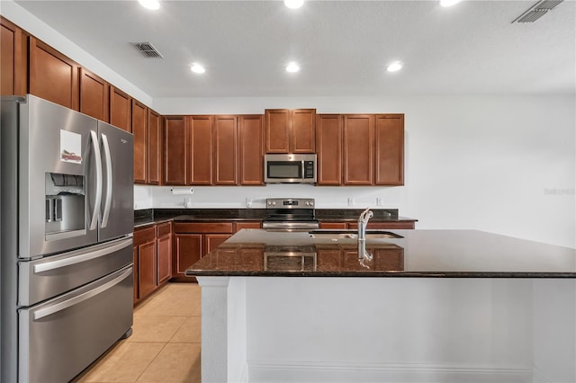 kitchen with light tile patterned floors, a kitchen island with sink, dark stone countertops, sink, and stainless steel appliances