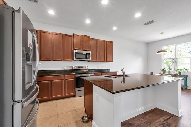 kitchen with an island with sink, light hardwood / wood-style flooring, stainless steel appliances, sink, and decorative light fixtures