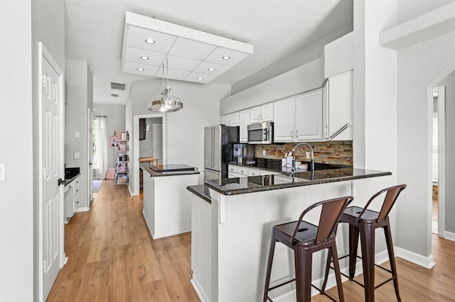 kitchen with kitchen peninsula, pendant lighting, stainless steel appliances, and light hardwood / wood-style flooring