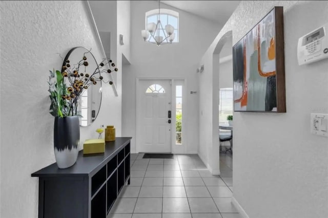 tiled entrance foyer featuring an inviting chandelier and high vaulted ceiling