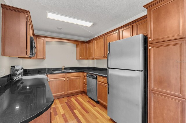 kitchen with appliances with stainless steel finishes, brown cabinets, a textured ceiling, light wood-style floors, and a sink