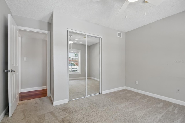 unfurnished bedroom featuring a textured ceiling, carpet flooring, visible vents, baseboards, and a closet