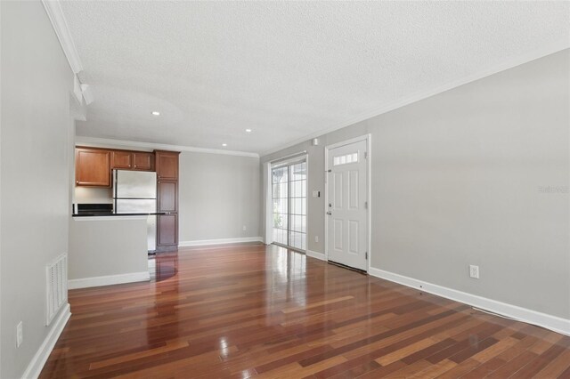 unfurnished living room with ornamental molding, visible vents, dark wood finished floors, and baseboards