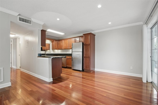 kitchen with stainless steel appliances, visible vents, light wood-style floors, ornamental molding, and dark countertops