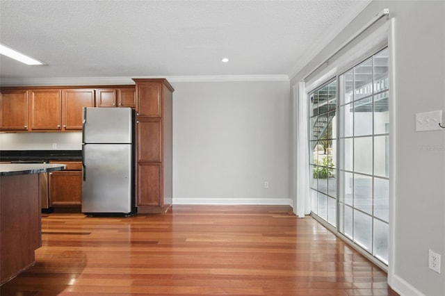 kitchen featuring ornamental molding, freestanding refrigerator, brown cabinetry, and dark countertops