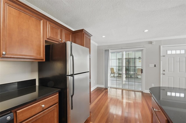 kitchen featuring wood-type flooring, freestanding refrigerator, brown cabinetry, dark countertops, and crown molding