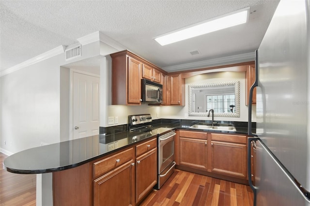 kitchen with stainless steel appliances, a sink, a peninsula, and wood finished floors